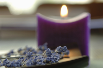 Lila Kerze flackert und Lavendel im Vordergrund zur Stimmung