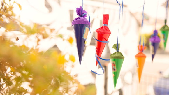 Kleine Deko-Schultüten hängen im hellen Raum, vorne links sind unscharf Blätter eines Baumes oder Busches im Vordergrund zu sehen