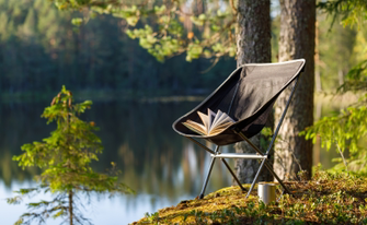 ein buch auf klappstuhl am see zum thema camping essentials