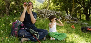 Papa und Kind mit Fernglas auf einer Wiese vor einem Wald