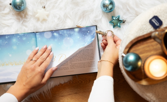 Aufgeschlagenes Buch "Das Geheimnis von Asfjördur" in weihnachtlichem Ambiente passend zum Buch, eine Hand schneidet mit einem Brieföffner die Seiten auf