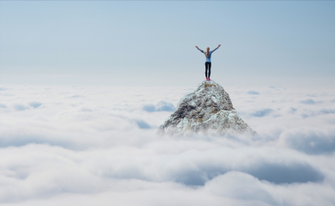 Eine Person steht mit erhobenen Armen auf einem Berggipfel, der aus einer Wolkendecke ragt.