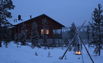Verschneites rustikales Haus in der Abenddämmerung, draußen und drinnen brennt ein Licht, gemütliche ruhe Atmosphäre