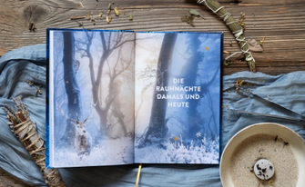 Aufgeschlagenes Buch mit Doppelseite im winterlichen Wald auf mystischen Hintergrund. Es ist Räucherwerk und eine Brennschale zu sehen auf einem blauen Tischläufer
