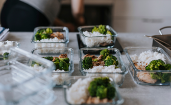 Vorbereitete Mahlzeiten (Meal Prep) in Glasbehältern auf einer Küchenzeile, bestehend aus gesundem gedünstetem Brokkoli, Reis und gebratenem Hähnchenbrustfilet.