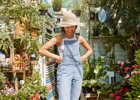 Frau steht positiv gestimmt im Garten, um sie herum viele Pflanzen und Blumen