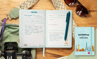 Stillleben einer Reisevorbereitung auf einer Holzoberfläche. Im Zentrum liegt ein aufgeschlagenes hellblaues „Reisetagebuch Städtetrips“, in dem handschriftliche Notizen zu einem Trip nach Barcelona im März 2026 zu sehen sind. Rechts daneben ist das geschlossene Buch mit einer Skyline-Illustration (u. a. Eiffelturm, Big Ben) abgebildet. Die Szene wird durch Reiseutensilien wie eine Sonnenbrille, eine Kamera, eine grüne Umhängetasche mit gemustertem Gurt und farblich passende Stifte ergänzt.