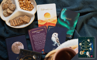 Auf einer dunklen Decke liegen mehrere Karten mit Nachtmotiven wie einer Eule und Polarlichtern, eine Box des Kartensets „Die geheimnisvolle Weisheit der Nacht“, Gebäck und Nüsse auf einem Teller.