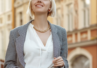Abbildung einer jungen Frau mit blonden Haaren, weißer Bluse und einem karierten Blazer, die lächelt