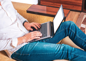 Mann in blauer Jeans und weißem Hemd sitz in einem Sessel mit einem Laptop auf dem Schoß