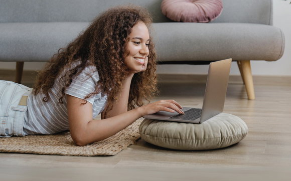 Eine Frau liegt bäuchlings auf dem Boden und schaut auf einen Laptop.