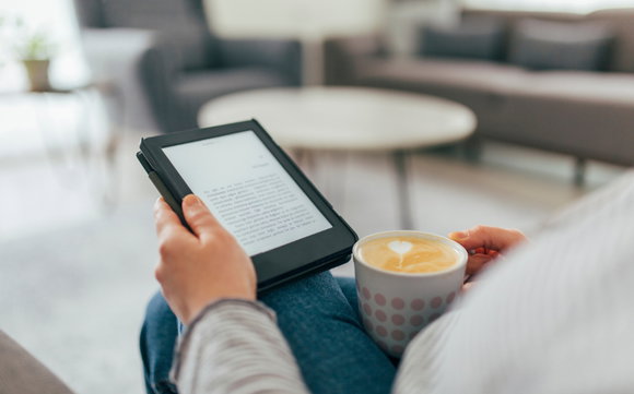 Closeup: Eine Hand hält den E-Reader, die andere einen Kaffee