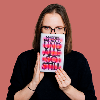 Eine Frau im schwarzen Pulli und mit großer dunkler Brille hält «Und alle so still» von Mareike Fallwickl vor den Mund