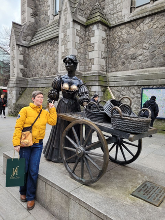 Bronzestatue von Molly Malone, die einen Handwagen auf zwei Rädern schiebt, au fdme sich geflochtene Körbe liegen