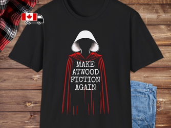 Ein schwarzes T-Shirt, darauf das ikonische Bild einer der Frauen aus "The Handmaids Tale" mit weißer Haube und roter Robe. In der Mitte steht "Make Atwood Fiction Again"