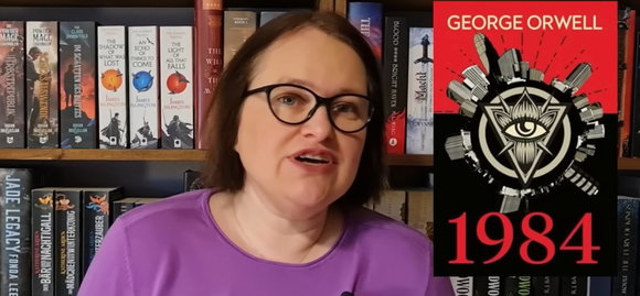 Eine Frau mittleren Alters mit halbem Oberkörper und Kopf vor einer Bücherwand, die braunen Haare halblang, dazu eine Brille. Rechts von ihr eingeblendet ein Cover von George Orwells 